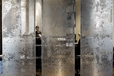 a woman is sitting on a bench in front of some metal partitions with holes