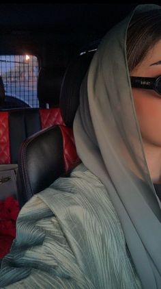 a woman wearing sunglasses is sitting in the back seat of a car with her head covered by a scarf