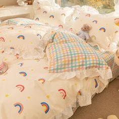 a teddy bear sitting on top of a bed with white sheets and rainbow print pillows