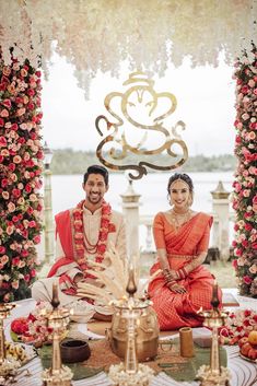 a man and woman sitting in front of a table with flowers on it, posing for the camera