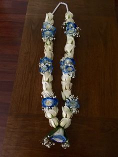 a necklace with blue and white flowers hanging from it's side on a wooden table