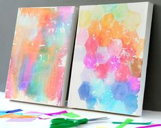 two colorful paintings on canvases with crayons and paintbrushes next to them