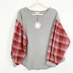 a gray shirt with red and white flannel sleeves on a hanger against a white wall