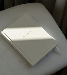 a white book sitting on top of a white chair next to a window with the sun shining through it