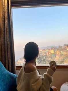 a woman sitting in front of a window holding a cup