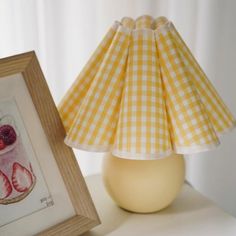 a yellow lamp shade sitting on top of a table next to a picture frame and painting