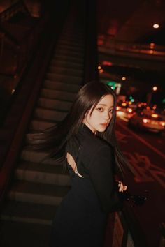 a woman with long black hair standing on stairs in front of a building at night