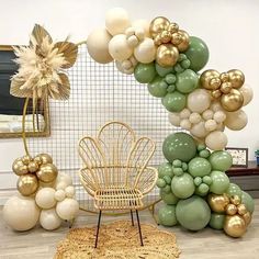 balloon arch with gold and green balloons on the floor next to a wicker chair