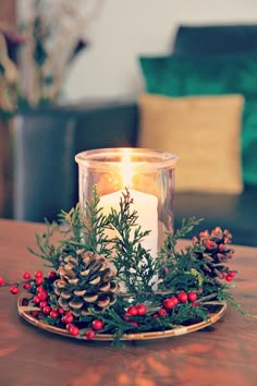 a candle sitting on top of a wooden table next to a christmas wreath and pine cones