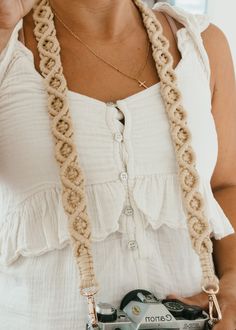 a woman holding a camera and wearing a crocheted chain around her neck, in front of a window