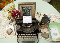 an old fashioned typewriter sitting on top of a table next to some books and flowers