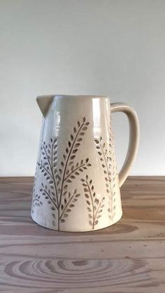 a cream colored pitcher sitting on top of a wooden table next to a white wall