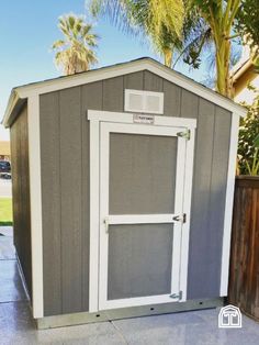 a gray and white shed sitting on top of a cement floor next to a tree