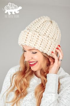 a woman wearing a white knitted beanie with red nail polish holding her hand up to her ear