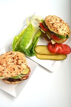 two plates with sandwiches and pickles on them sitting next to each other in front of a white background