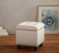 a white ottoman sitting on top of a hard wood floor next to a framed painting