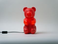 a red plastic teddy bear sitting next to a black cord on a white table top