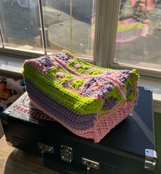 a crocheted bag sitting on top of an open suitcase next to a window