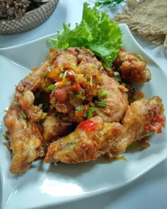 a white plate topped with chicken wings covered in sauce and garnished with lettuce