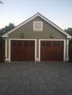 two brown garage doors are on the side of a gray and white house with brick driveway