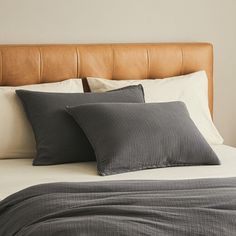 two pillows on top of a bed with white sheets and brown leather headboard in a bedroom