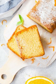 two slices of orange pound cake sitting on top of a cutting board next to an orange slice