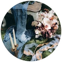 a bouquet of flowers sitting on the ground next to a pair of jeans and a candle