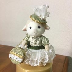 a small white stuffed animal wearing a dress and holding a purse on top of a table