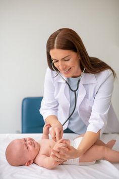 a woman in white shirt and stethoscope examining a baby