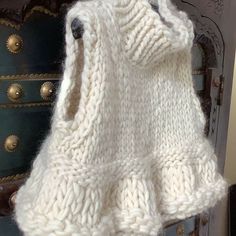 a white knitted sweater hanging from a hook on a wooden door frame with brass knobs