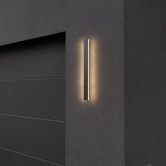 a modern wall light on the side of a building with an open garage door in front of it