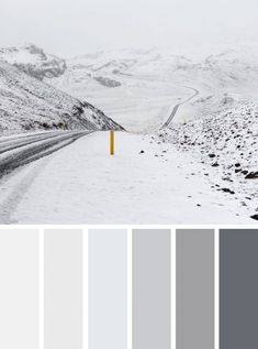 a snowy road with mountains in the background and a yellow post at the end that is surrounded by snow