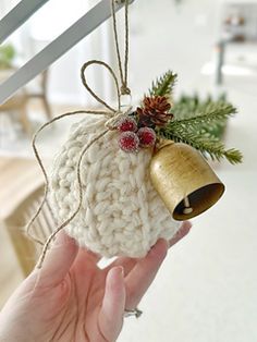 a hand holding a small christmas ornament with a bell on it's side