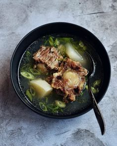 a bowl filled with meat and vegetables on top of a white countertop next to a spoon