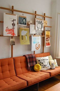 an orange couch sitting in front of a window next to a wooden shelf with pictures on it