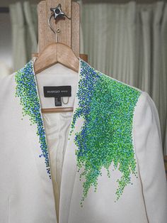 a white jacket with green and blue sprinkles hanging on a wooden hanger