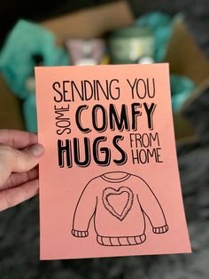 someone holding up a card that says sending you comfy hugs from home