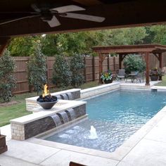 a backyard with a swimming pool and fire pit surrounded by greenery in the back yard