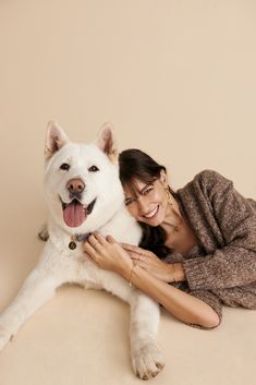 a woman laying on the floor with her white dog and smiling at the camera,