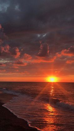 the sun is setting over the ocean with clouds in the sky and waves on the beach