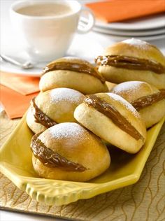 small pastries on a yellow plate next to a cup of coffee and orange napkins