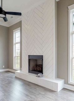 an empty living room with a fireplace and two windows in the wall, along with hardwood flooring