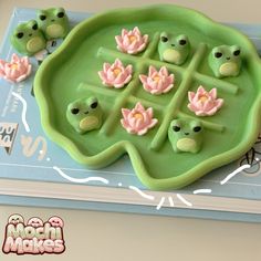 a green tray with pink flowers and frog faces on it sitting on top of a book