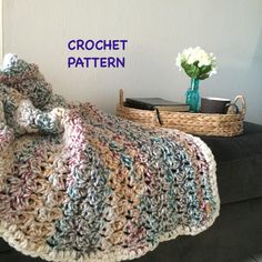 a crocheted blanket sitting on top of a couch next to a basket with flowers