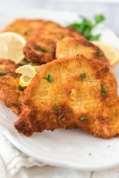 some fried food on a white plate with lemon wedges