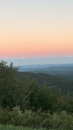 the sun is setting in the distance over the hills and trees on the hill side