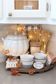 the kitchen counter is decorated with white dishes and pumpkins, wheat stalks, and lights