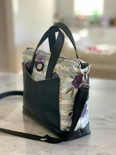 a handbag sitting on top of a marble counter next to a black bag with purple flowers