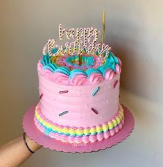 a birthday cake with pink frosting and sprinkles is being held by a person