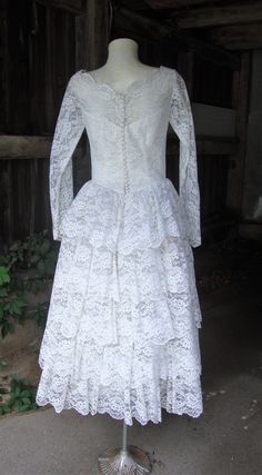 "This is a white lace and tulle full skirt wedding dress from the 1950's. The dress features a wide neckline with scalloped edges embellished with seed pearls and iridescent sequins. The sleeves are fitted and end in bridal points, opening with covered buttons and loops at the wrists. This dress opens down the back with covered buttons and loops and they are all there. The skirt is very full, with a multi tiered ruffled back. Under the lace layer is a full layer of tulle, and then an underskirt Vintage Lace Petticoat With Ruffles, Vintage Wedding Dress With Attached Cancan, Vintage Lace Wedding Dress With Lace Bodice, Vintage Lace Dress With Lace Bodice For Wedding, Vintage White Lace Petticoat, Vintage Scalloped Lace For Wedding, Vintage Fitted Petticoat For Wedding, Vintage Fitted Wedding Petticoat, Lace Ruffled Petticoat For Wedding